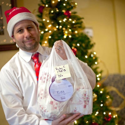 https://www.beasantatoasenior.com/siteassets/volunteer-dressed-in-holiday-attire-holds-bag-of-donated-gifts-for-senior.jpg